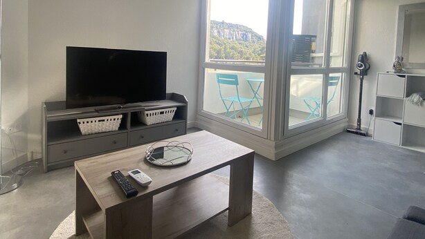 Uma sala de estar moderna com uma TV de tela plana, uma mesa de centro de madeira e vista para uma varanda com móveis de exterior.