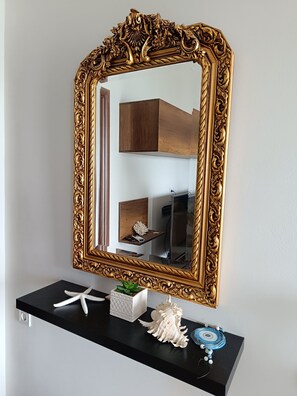 A mirror with an ornate gold frame, a black console table, and decorative items including a starfish and a seashell.