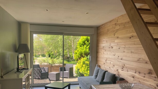 Un salon moderne avec un canapé, une table à manger et une petite table basse. Une grande fenêtre offre une vue sur un jardin.