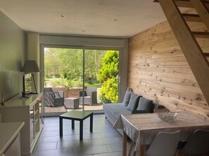 Een moderne woonkamer met een bank, een eettafel en een kleine salontafel. Een groot raam biedt uitzicht op een tuin.