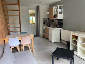 A compact living space with a kitchenette, a dining area with a table and chairs, a sofa, and a small black table. - Gîte de Kermoal-Maison 2 chambres (Poullan-sur-Mer)