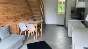 Un intérieur moderne avec une chambre à coucher aménagée en mezzanine, un coin repas avec une table et des chaises en bois, un coin cuisine et un canapé gris.