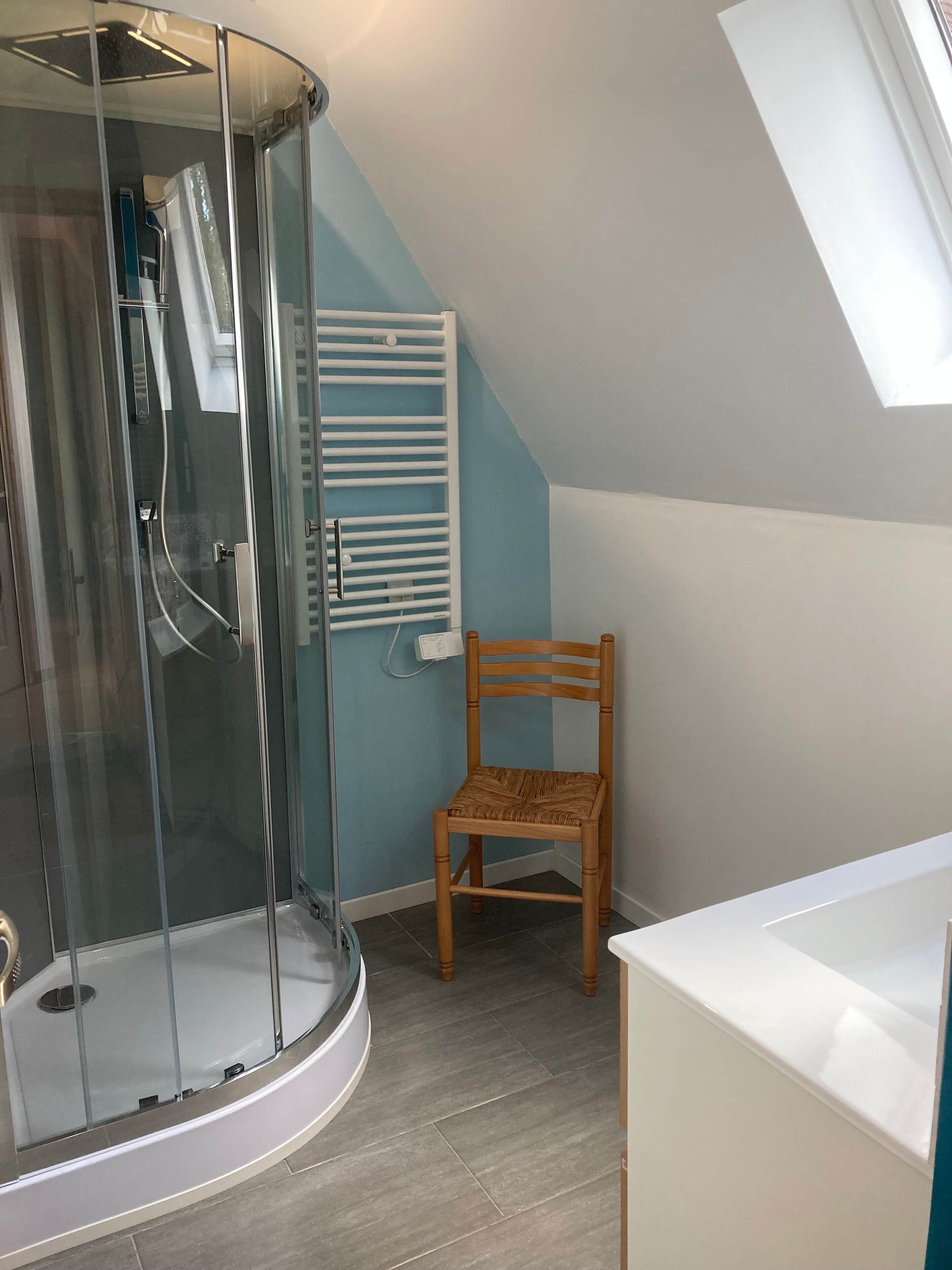 A shower with a glass door, a wooden chair, and a white sink.