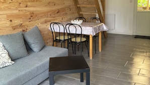 Un salon moderne avec un plafond en pente en bois, un canapé gris, une table à manger avec des chaises et une petite table noire.