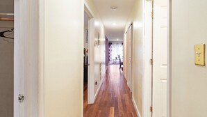 Un couloir étroit, doté d’un plancher en bois et de murs blancs, qui mène à une pièce dont la porte se trouve au fond.