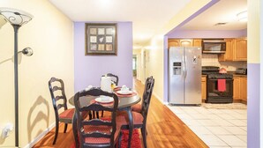 Une cuisine compacte dotée d’appareils électroménagers modernes, un coin repas avec une table dressée pour quatre personnes, et un couloir menant aux autres pièces.
