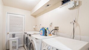Une buanderie équipée de deux machines à laver, d’un sèche-linge, d’un évier et d’une poubelle.