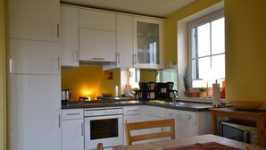 Eine Küche mit weißen Schränken, einem Holztisch und einem Fenster.