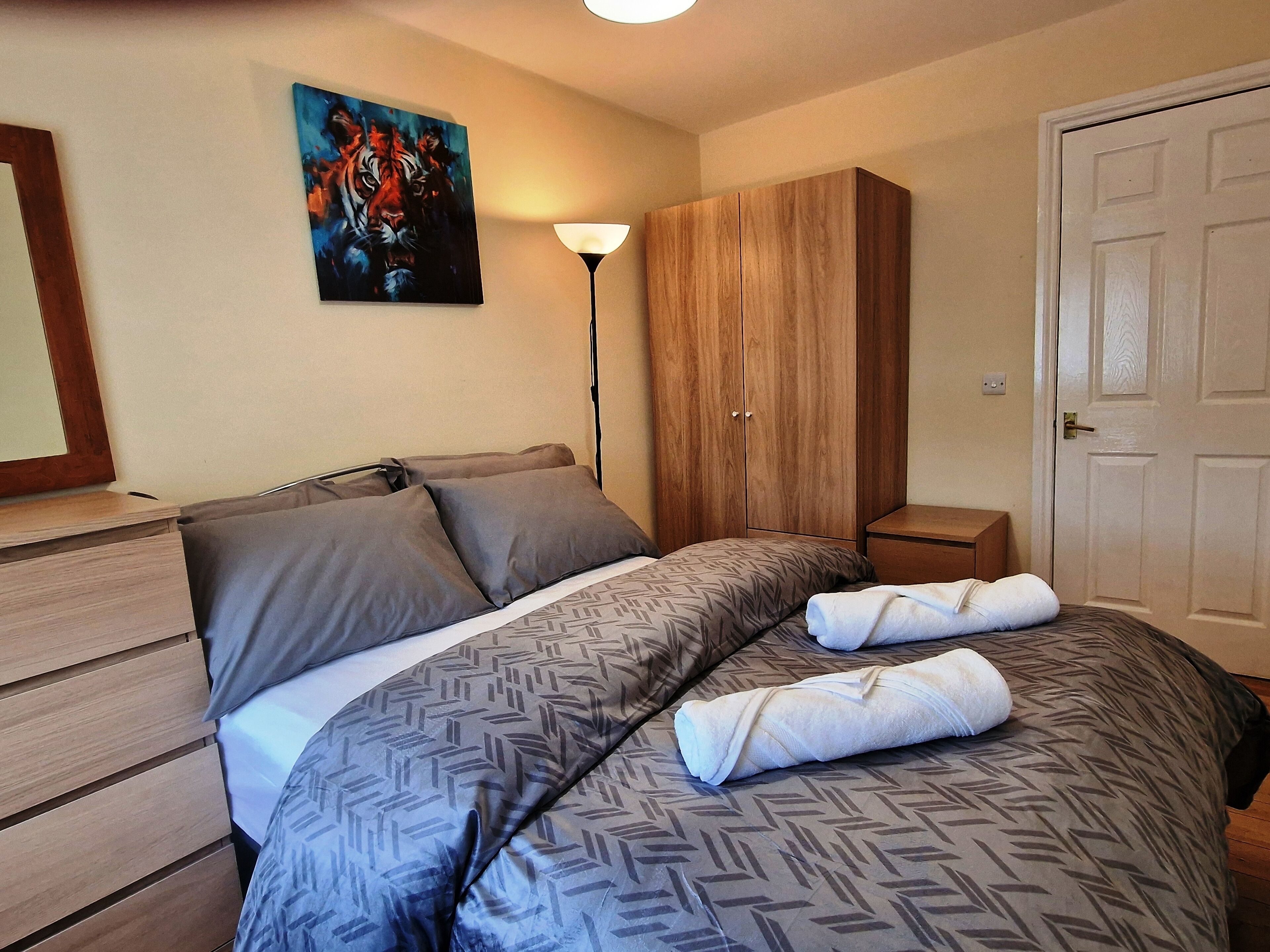A bedroom with a bed, a wardrobe, a nightstand, a lamp, and a door.