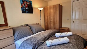 Ein Schlafzimmer mit Bett, Schrank, Nachttisch, Lampe und Tür.