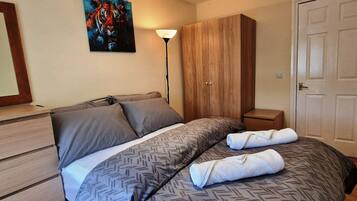 A bedroom with a bed, a wardrobe, a nightstand, a lamp, and a door.