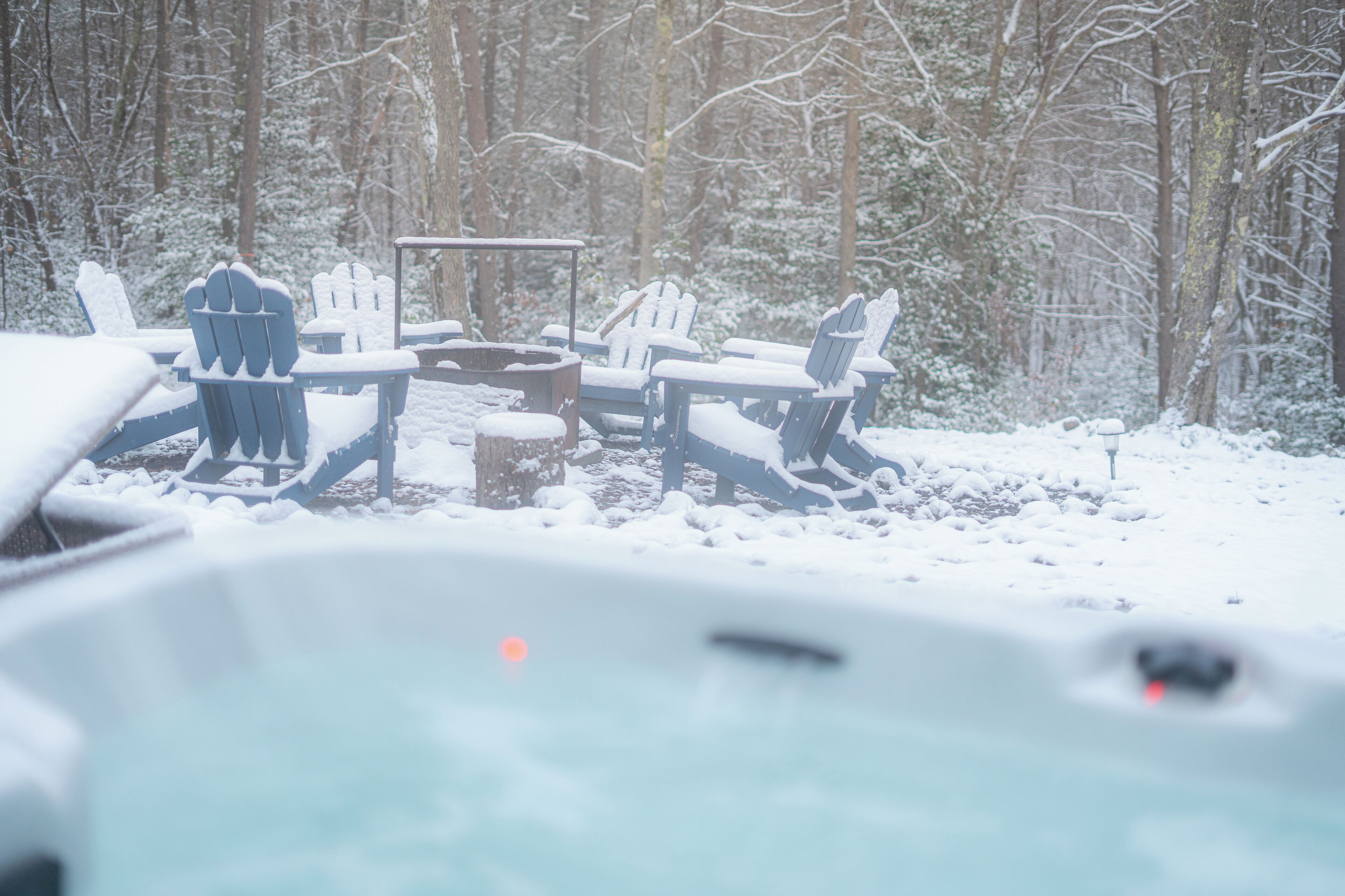 A snow-covered outdoor seating area with Adirondack chairs and a fire pit.