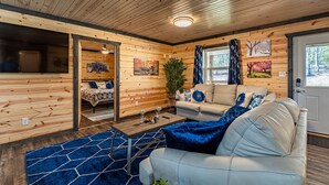 L’intérieur d’un chalet accueillant, avec des murs en bois, un canapé, une table basse et un lit recouvert d’une courtepointe à motifs.