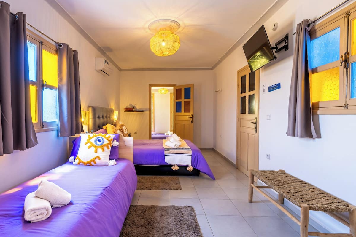 A hotel room with two beds, a bench, and a hallway leading to another room.