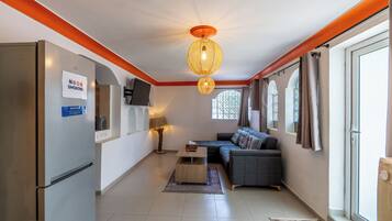 Um espaço compacto com sofá, televisão na parede, luminária no teto e janela com cortinas.