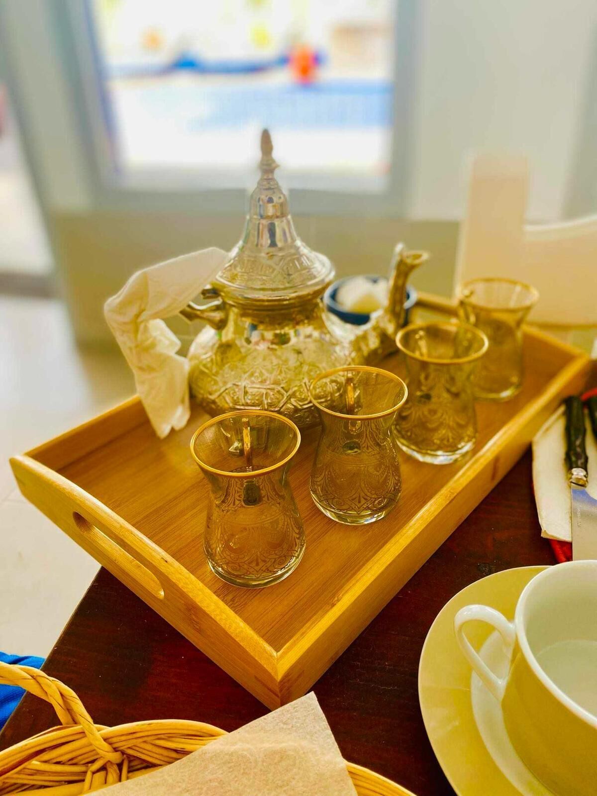 Una bandeja con una jarra de vidrio, cuatro vasos y una taza sobre una mesa de madera.