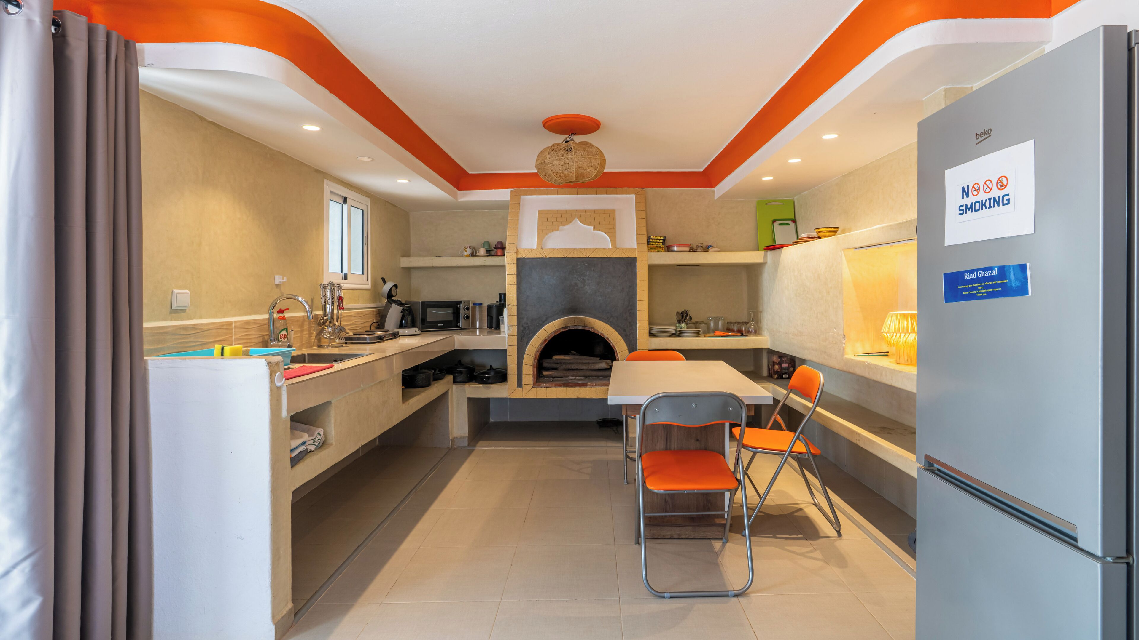 Een kleine keuken met een inbouwoven, een koelkast en een eethoek met stoelen.