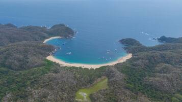 An aerial view of a coastal area with a beach, boats, and forested hills.