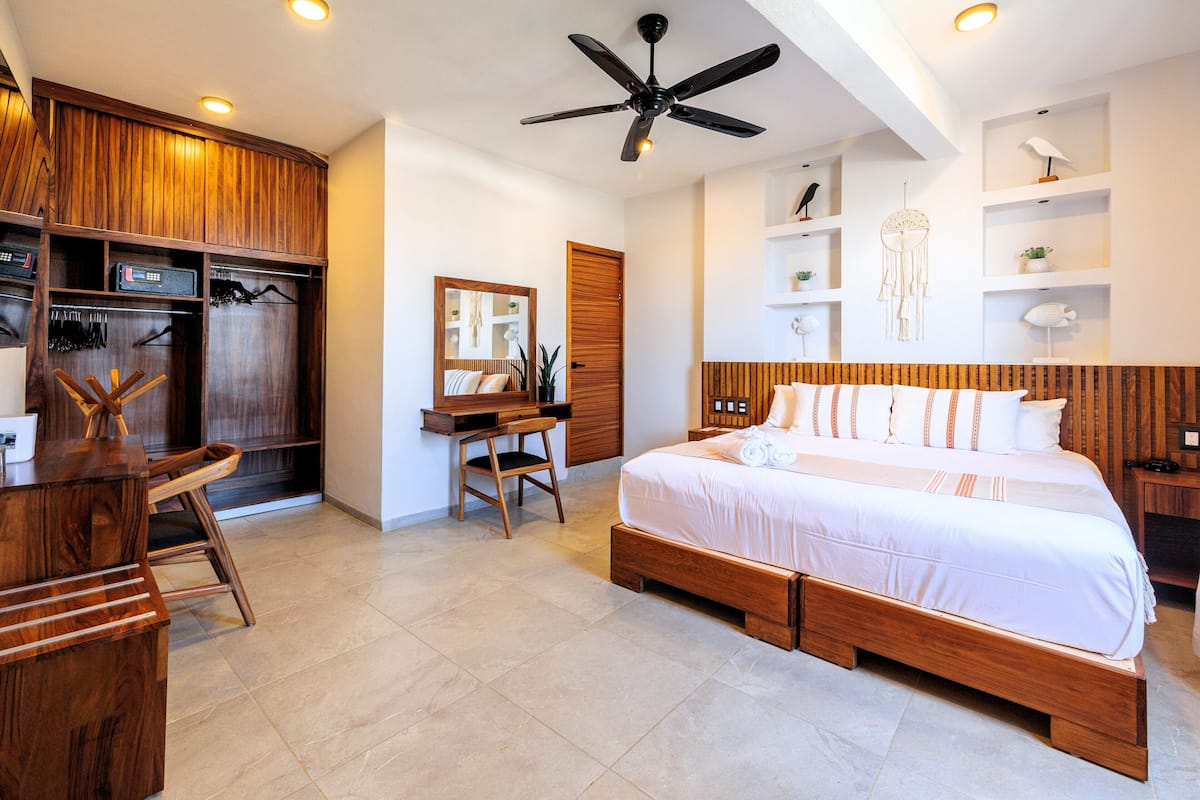 A bedroom with a large bed, wooden wardrobe, desk, and a ceiling fan.