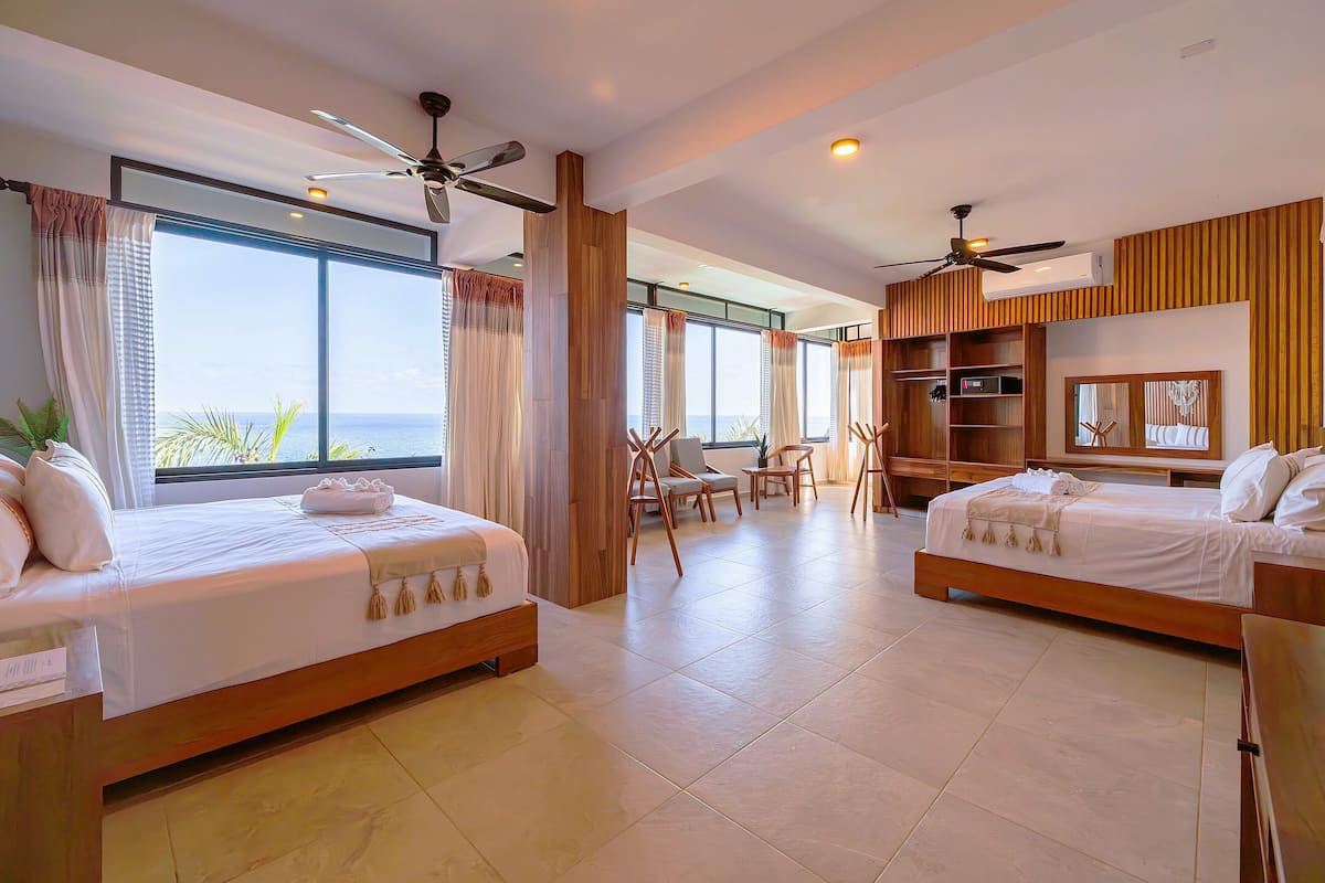 A hotel room with two beds, a dining area, and a view of the ocean.
