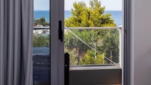 Un dormitorio con cama, puerta corrediza al balcón y vistas al mar y al verdor.