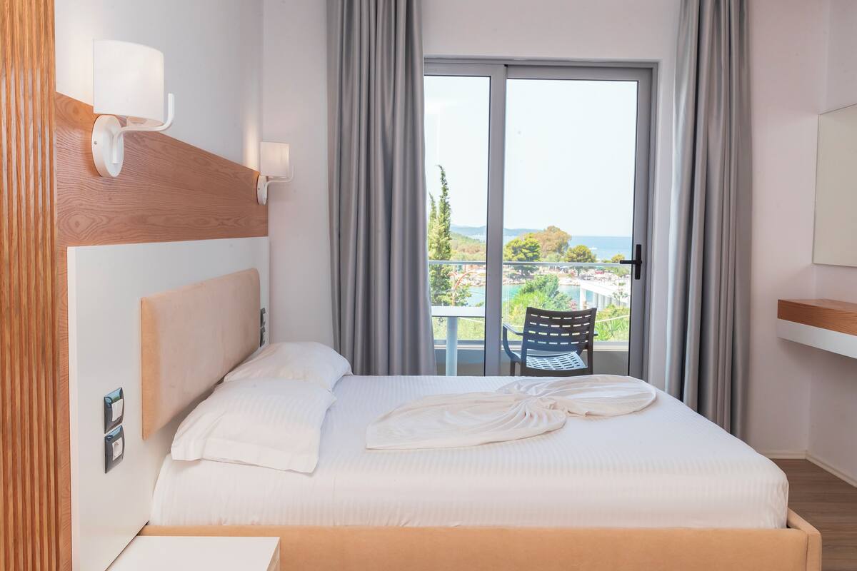A hotel room with a bed, a chair, a view of the outdoors, and a window with curtains.