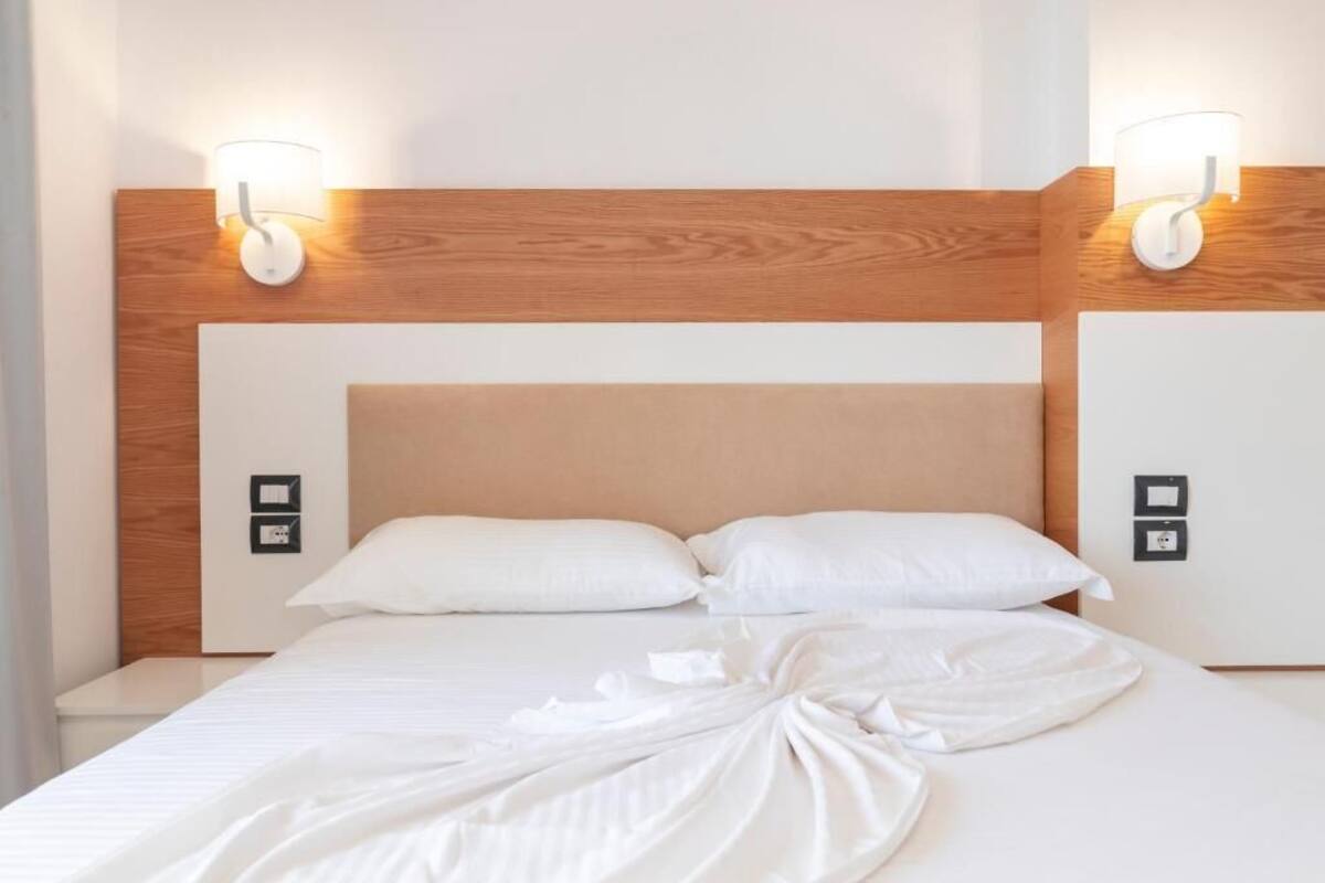 A hotel room with a wooden headboard, two bedside lamps, and a neatly made bed with white linens.