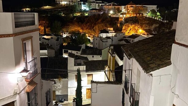 Vue nocturne d’un quartier résidentiel avec des bâtiments blancs, un escalier et une structure illuminée en arrière-plan.