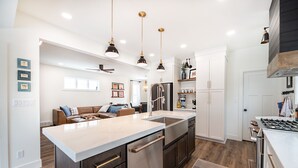 Une cuisine moderne dotée d’un îlot central, d’appareils électroménagers en acier inoxydable et de luminaires suspendus.