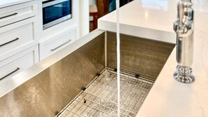 Une cuisine moderne dotée d’un évier en acier inoxydable, de meubles blancs et d’un luminaire suspendu.