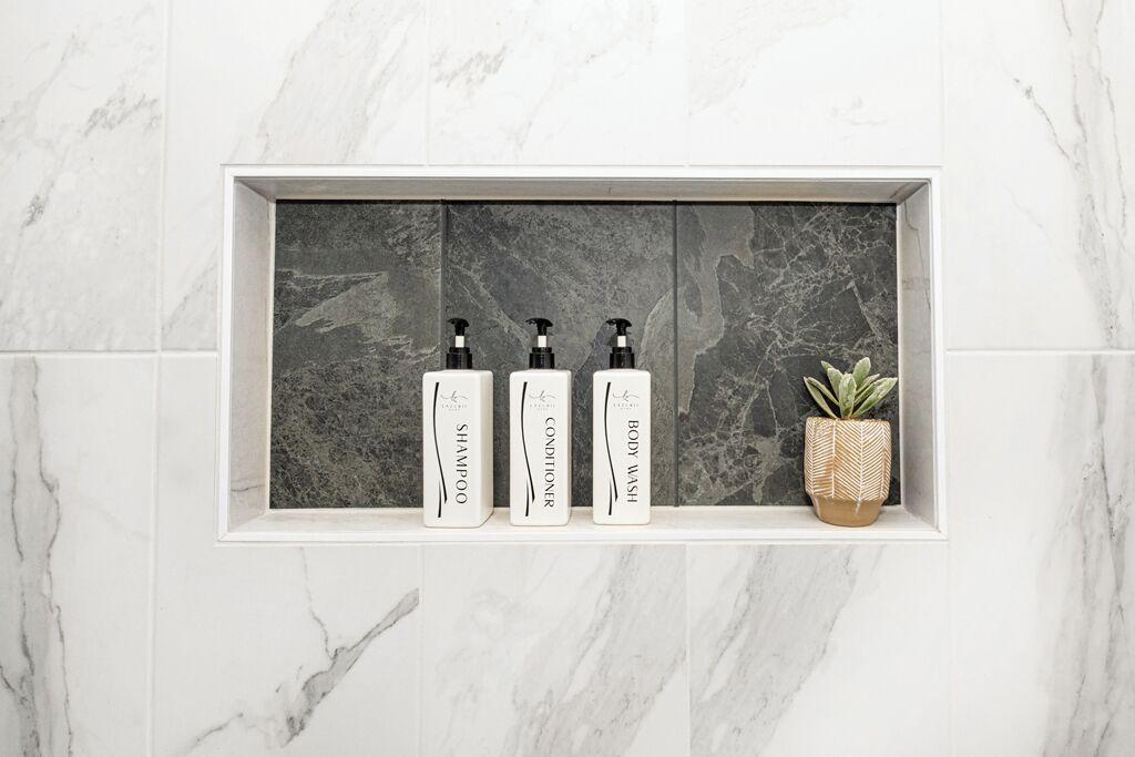 Ein Badezimmerschrank mit drei Flaschen Shampoo, Conditioner und Duschgel, sowie einer kleinen Topfpflanze.