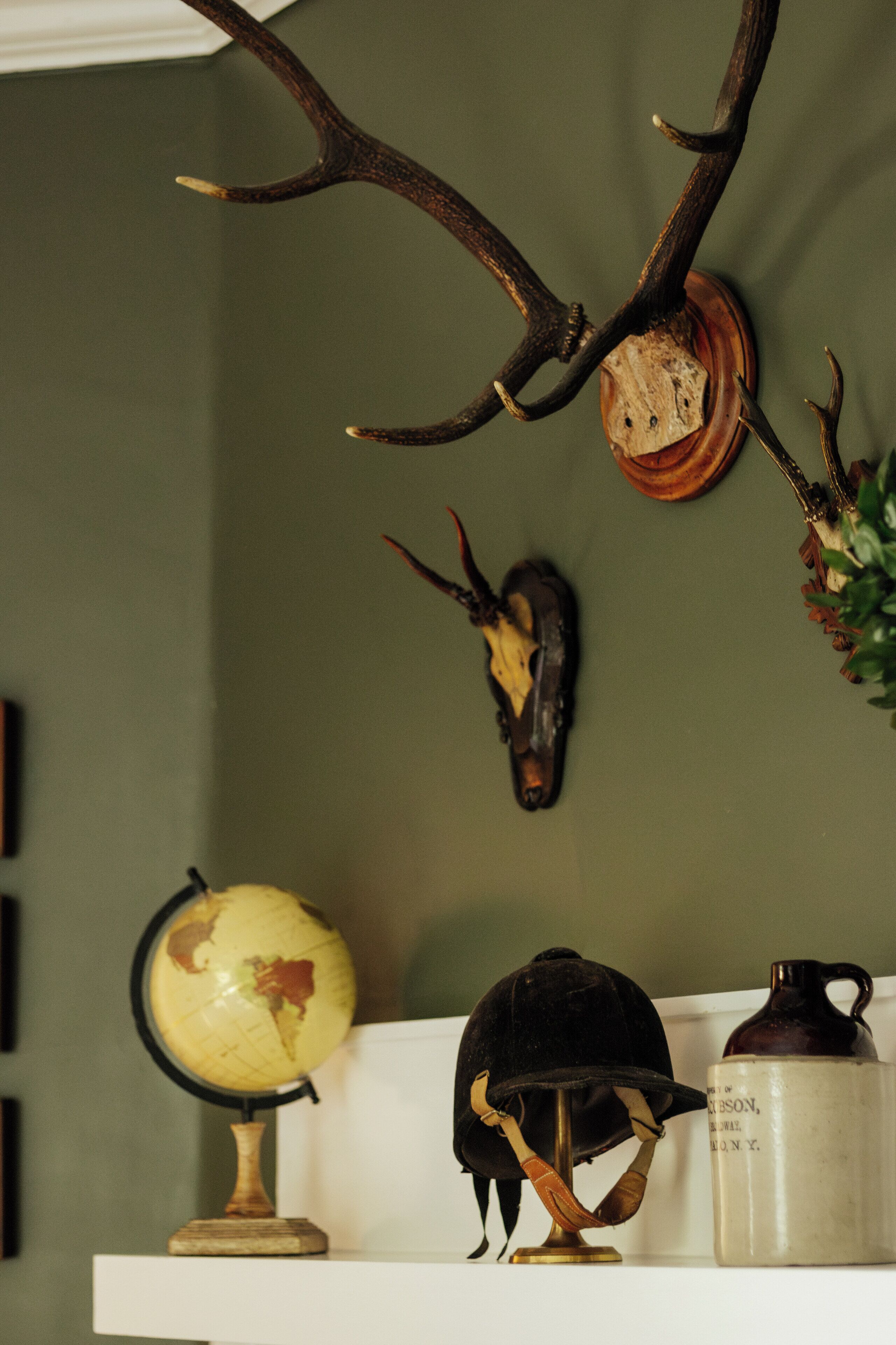 A shelf with a globe, a helmet, a ceramic pitcher, and antler displays.