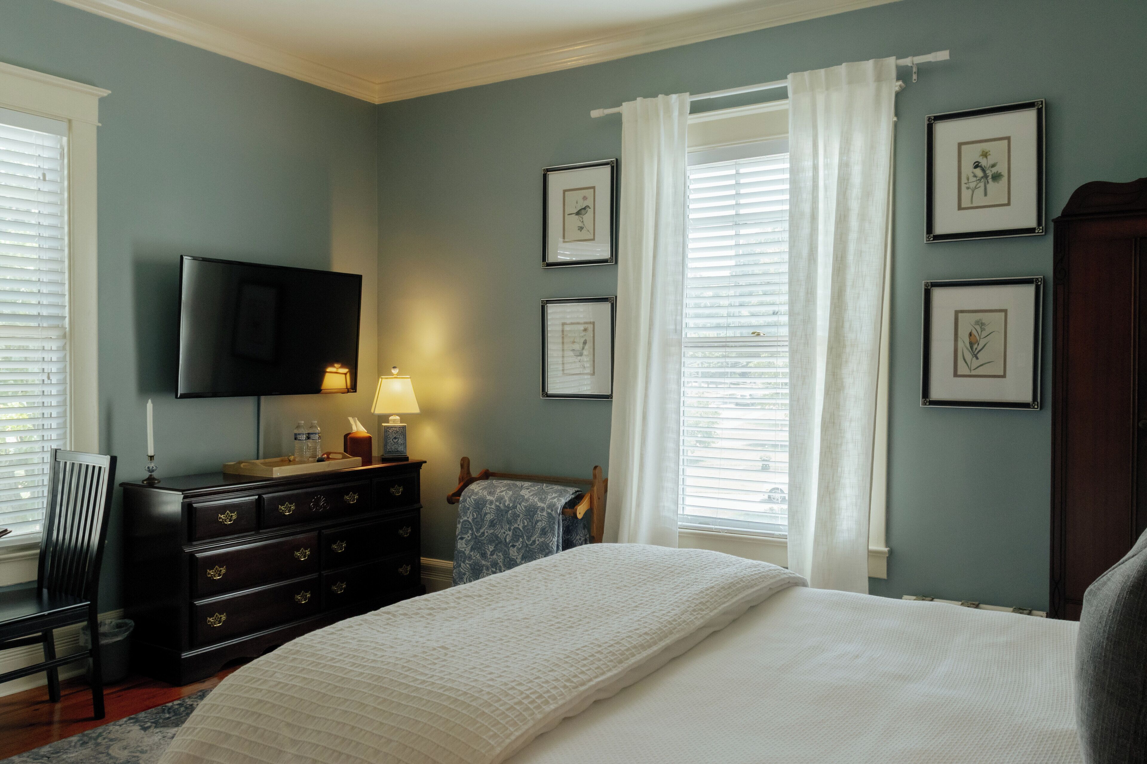 Un dormitorio con cama, cómoda, televisor y cuadros en la pared.