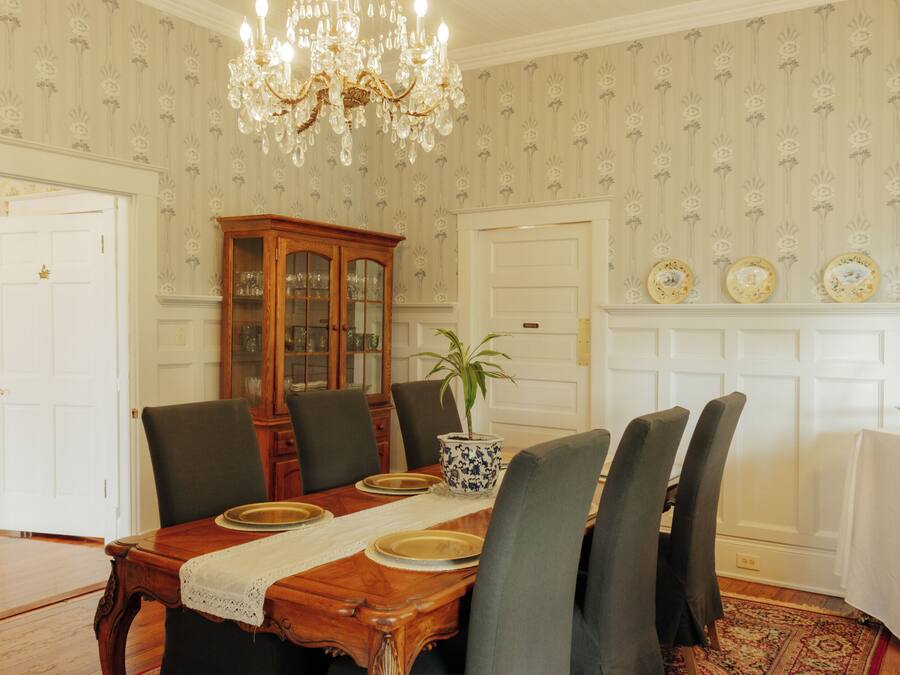 Un comedor con una mesa de madera, sillas, una lámpara de araña, un aparador y una planta en maceta.