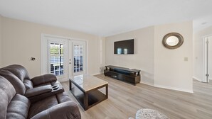 A living room with a leather sofa, a glass coffee table, a dark wooden TV stand, and a round mirror on the wall. - Centrally Located, Serene Luxury Retreat (Brandon)
