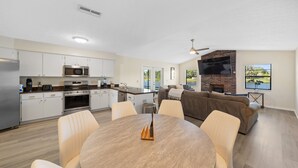 A modern kitchen with white cabinets, a microwave, and a dining area with a round table and chairs. There is a fireplace and a TV mounted on the wall. - Centrally Located, Serene Luxury Retreat (Brandon)