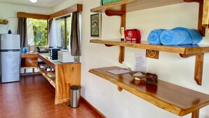 A kitchen with wooden shelves, a first aid kit, and a welcome sign. - The Fruit Tree Garden Bromeliad Suite (Arenal)
