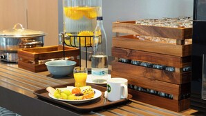 A breakfast buffet setup with a fruit tray, a juice dispenser, and a coffee station. - B&B Hotel Bremen-altstadt (Bremen)