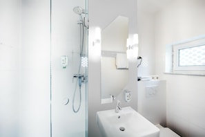 A modern bathroom with a glass shower enclosure, a white sink, a mirror, and a window with a view. - B&B Hotel Bremen-altstadt (Bremen)