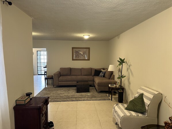 A living room with a sectional sofa, a small table with a lamp, a floor lamp, and a painting on the wall. - Beautiful entire home near Plaza Patio Mall (Saltillo)