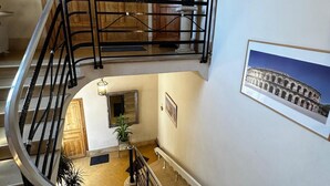 A multi-level interior with a staircase, wooden doors, a potted plant, and a framed picture of a historical building.