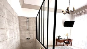 A modern bathroom with a shower, a towel rack, and a bed with a patterned bedspread.