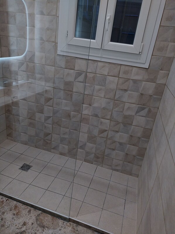 A bathroom with a tiled floor and walls, a window with a white frame, and a shower area.