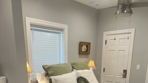 A bedroom with a bed, nightstands, a lamp, a window with blinds, a door, and a wall-mounted picture. - Cozy Stylish Executive Studio, Great Downtown Pascagoula Location (Pascagoula)