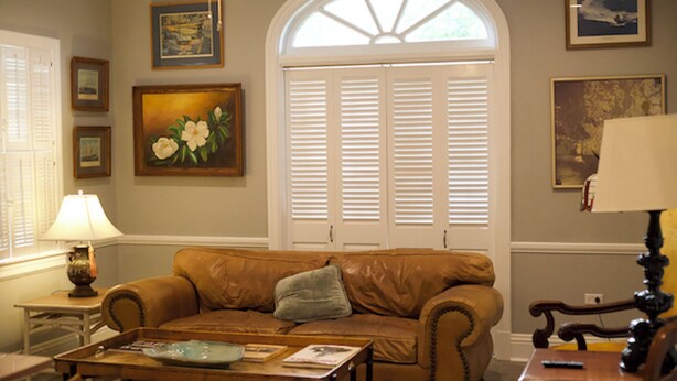 A living room with a brown leather sofa, a coffee table, a lamp, and a window with shutters. - Cozy Stylish Executive Studio, Great Downtown Pascagoula Location (Pascagoula)