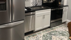 A modern kitchen with white cabinets, stainless steel appliances, a black countertop, and a patterned rug. - Cozy Stylish Executive Studio, Great Downtown Pascagoula Location (Pascagoula)