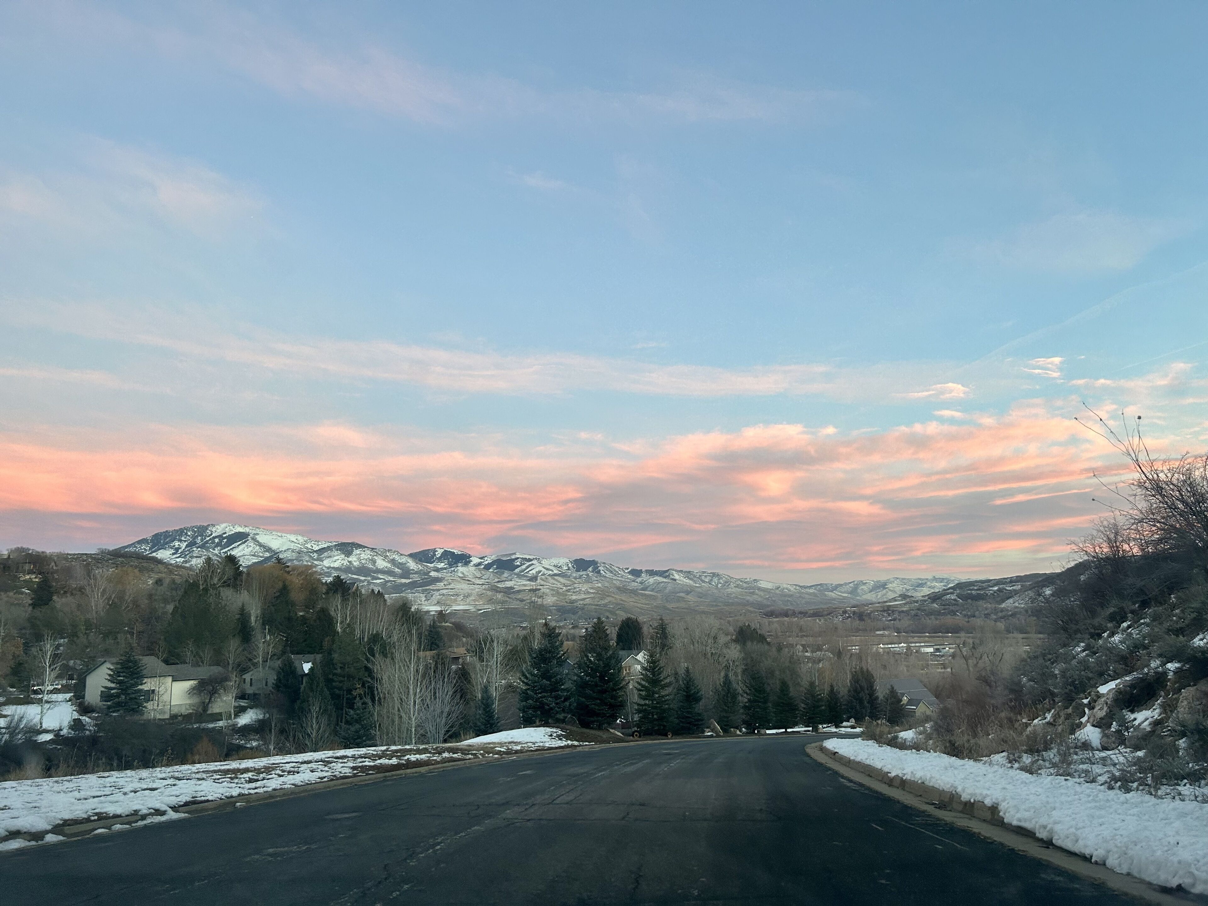 A road leading to a mountainous area with snow on the ground and trees lining the sides.
