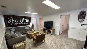 A living room with a sofa, coffee table, TV, and a sign that says "Ski Utah! Greatest Snow on Earth". - Cozy Mountain Retreat - Snowbasin, Skiing, Biking, Hiking, Fishing (Morgan)