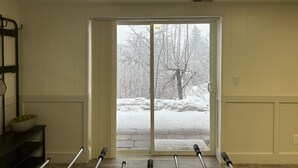 A room with a sliding glass door leading to a snowy outdoor area, a ceiling light, and a black metal rack with a bowl on the floor. - Cozy Mountain Retreat - Snowbasin, Skiing, Biking, Hiking, Fishing (Morgan)