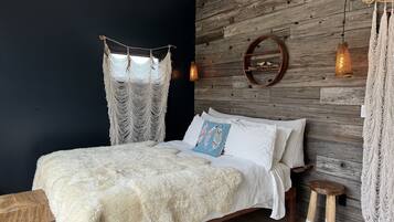 A bedroom with a bed, a wooden wall, a macrame curtain, a round mirror, and a hanging light fixture.